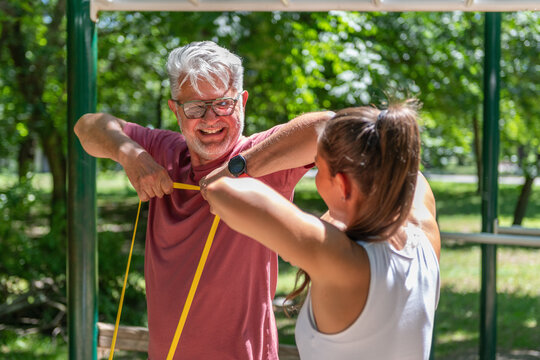 Senior man performing an upper body resistance band workout with a fitness coach to improve shoulder stability, muscular endurance, posture, and overall functional fitness.