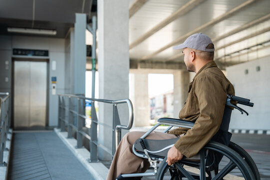 A man with a leg disability who cannot walk uses a wheelchair and travels by the train at a station He walks along the sidewalk where there are signs indicating accessibility for disabled individuals