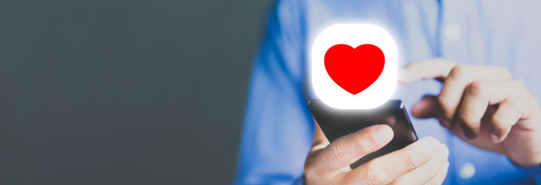 Man holding smartphone with red heart icon, online dating and social media engagement concept