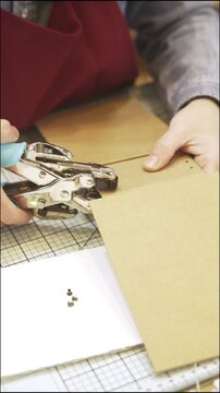 Person creating a scrapbook album and punching holes with tools