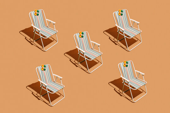 Striped beach chairs with pineapple sunglasses on orange background