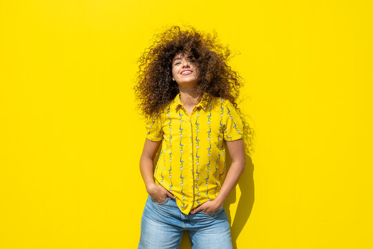 Smiling woman with curly hair and yellow shirt on yellow background
