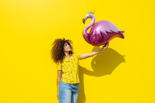 Smiling woman holding a pink flamingo balloon in summer sunlight