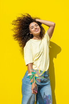 Smiling woman with curly hair holding a pinwheel in summer sunlight