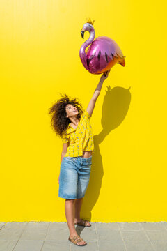 Woman holding a pink flamingo balloon against a yellow background in summer