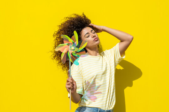 Smiling model with curly hair holding a pinwheel in summer sunlight