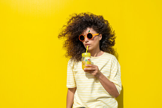 Smiling model with curly hair drinking juice in summer