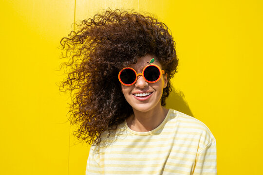 Smiling woman with curly hair and fruit sunglasses on yellow background