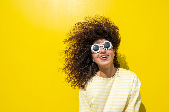 Smiling model with curly hair and sunglasses on yellow background