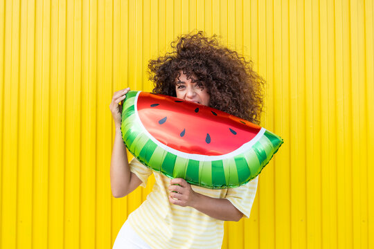 Woman holding a watermelon balloon against a bright yellow background