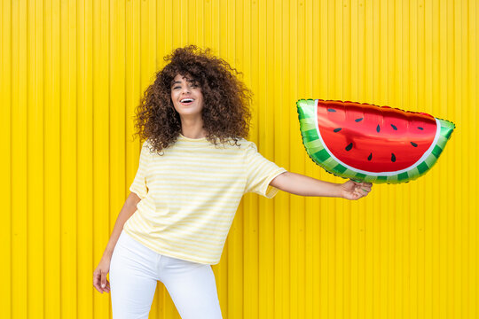 Smiling model holding a watermelon balloon on a yellow background