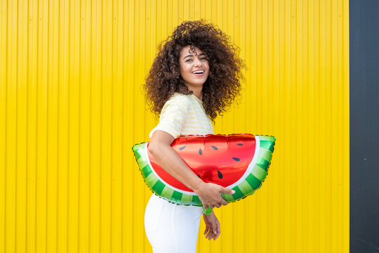 Smiling woman with a watermelon balloon against a yellow background
