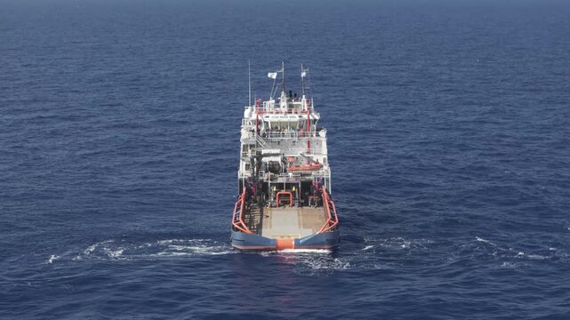 Drone perspective following the stern of an anchor handling tug supply vessel moving through deep blue sea waters