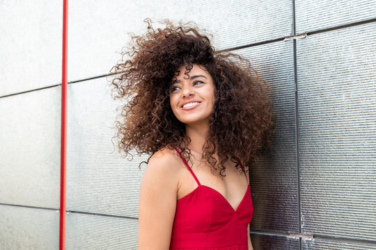 Smiling model with curly hair in a red dress looking away