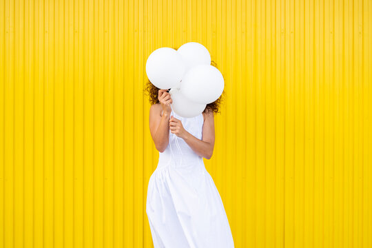 Female hiding face behind white balloon on yellow background