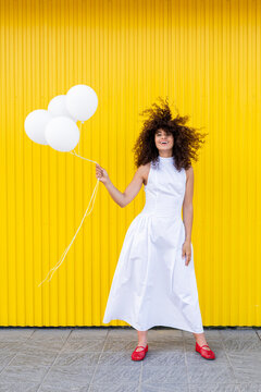 Happy female in white dress holds balloon against yellow background