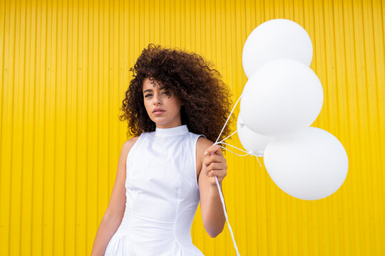 Woman in white dress holds white balloon on yellow background