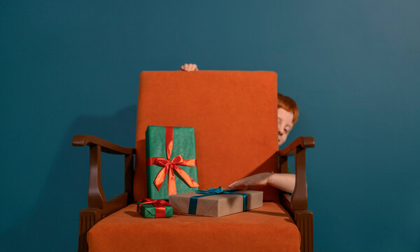 Red-haired child reaching for gifts on armchair indoors