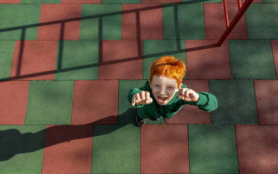 A happy red-haired boy reaches his hands toward the camera