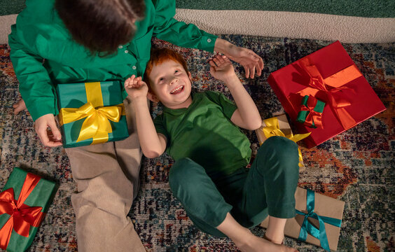 Red-haired boy lying on floor with mother and gifts at home