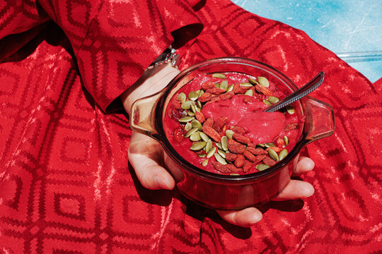Hand holding bowl of vegan beetroot soup with superfood topping