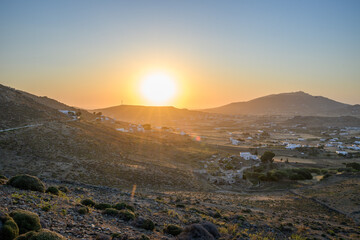 Obraz premium Sun rising over the hills and white houses of the Ano Mera valley in golden morning light, Mykonos, Greece 
