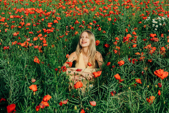 Woman sits in a summer poppy field enjoying freedom and nature