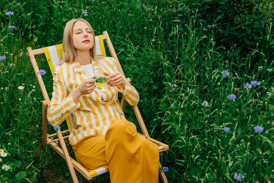 Woman in yellow jacket relaxes in wildflower garden drinking tea