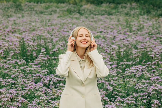 Woman in white suit listens to music in a purple flower meadow