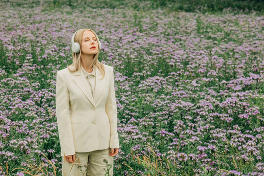 A woman in a white suit listens to music in a phacelia meadow