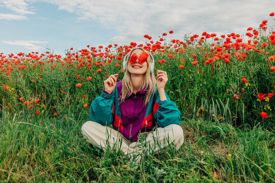 Smiling woman in retro tracksuit holds a poppy flower over her eye