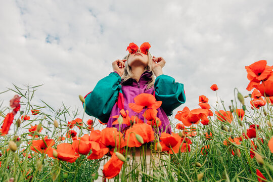 Woman in retro tracksuit covers eyes with red poppies in a meadow