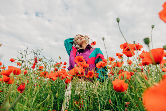 Woman in retro tracksuit listens to music in a red poppy meadow