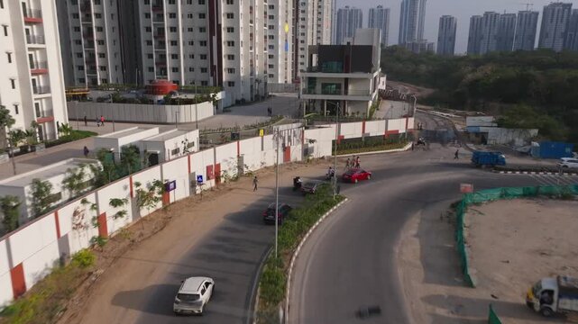 Vehicles moving on curved road with peoples, street lights and skyscraper at Makthakousarali, khajaguda, manikonda, hyderabad, telangana, india. day time, push in shot, drone shot, 4k.