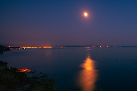 Full moon reflecting across the calm Adriatic Sea during blue hour with peaceful coastline creating a romantic atmosphere.