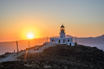 Armenistis Lighthouse on Mykonos at sunset with the sun setting over the Aegean Sea and a path leading up the hill, Cyclades, Greece © Michal Plevko