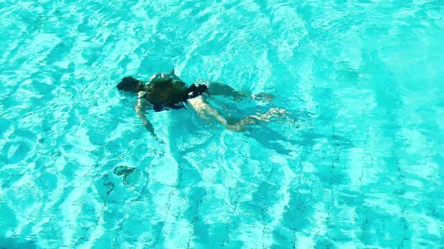 Girl in ablack swimsuit swims underwater in a clear blue pool. Idea summer fun, youth, physical activity, sports, freedom, and water activities.