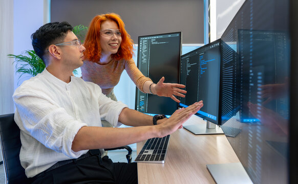 Two developer focus on coding at their desk, surrounded by multiple computer screen displaying line of code in a contemporary workspace, enhancing teamwork and creativity.