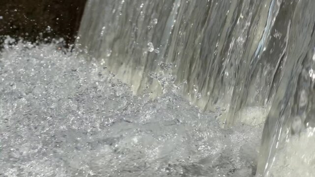 Artificial concrete check dam directs water into churning, frothy river stream lined with green trees.