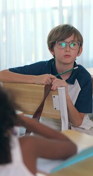 Schoolboy with glasses curiously watching his classmates secretly pass a paper note during a lesson.