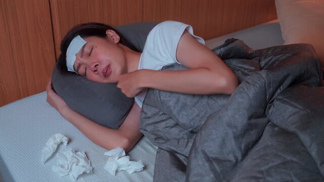 Pile of used tissues near a sleeping ill Asian female with a fever patch. Concept of seasonal virus, health symptoms, and nighttime rest for recovery at home.