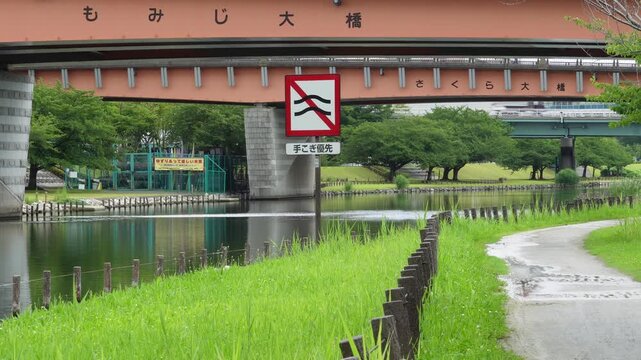 Serene walking path along the green riverbank of Kyu-Nakagawa River Park under Momiji-ohashi Bridge in Tokyo