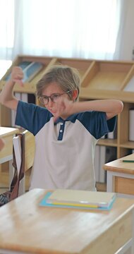 Playful schoolboy with glasses making funny faces and gestures to his classmates during a break.