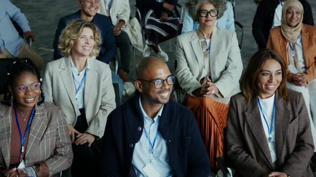 Diverse business professionals, wearing lanyards, happily attend a conference. They actively listen and smile, showcasing engagement and collaboration in a dynamic setting.