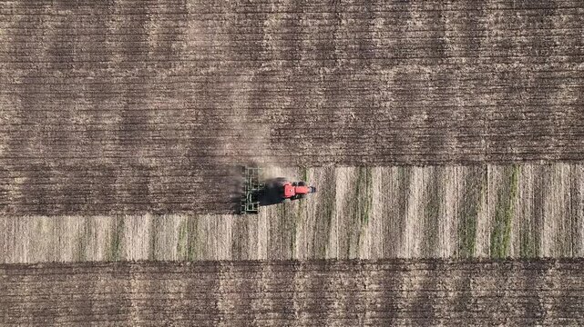 Drone rising above farmland with agricultural tractor at work, top view of field geometry, cultivated soil patterns and large scale farming landscape with copy space