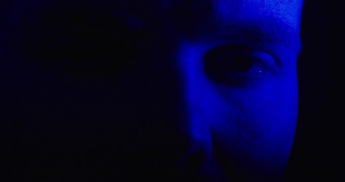Close-up of a person's face illuminated by flashing red police siren light against a dark background. Dramatic concept of crime, emergency, investigation, and suspense.