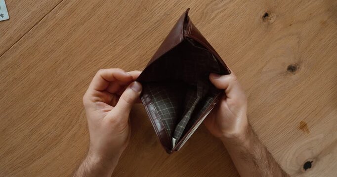 Top view of hands holding an empty wallet over a wooden table. Financial concept of no money, poverty, expenses, debt, and personal budgeting.