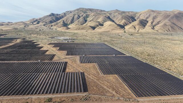 An aerial drone flies laterally past a utility-scale solar farm in the northern Nevada high desert, with dramatic barren hills rising steeply in the background.