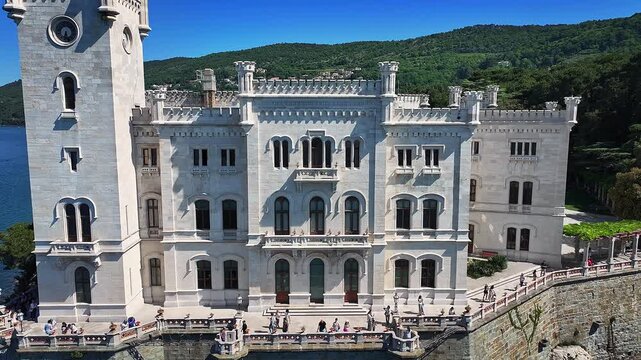 Trieste, Italy - 4K Flying away of the beautiful Miramare Castle (Castello di Miramare) by the Gulf of Trieste on a sunny summer day with blue sky and turqoise sea water