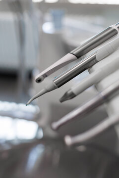 Close-up of metal dental handpieces on a treatment unit in a clean clinic, with shallow focus and soft blurred background